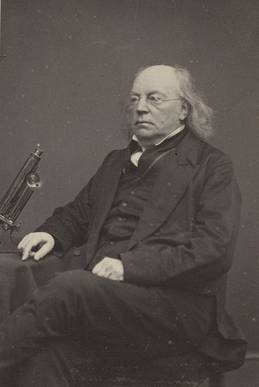 A black and white photo of Miles Joseph Berkeley sitting next to a microscope